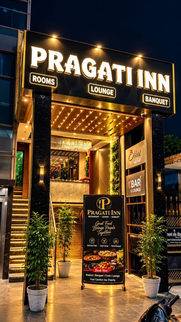 Exterior del Pragati Inn con señalización iluminada para habitaciones, salón y salas de banquetes.