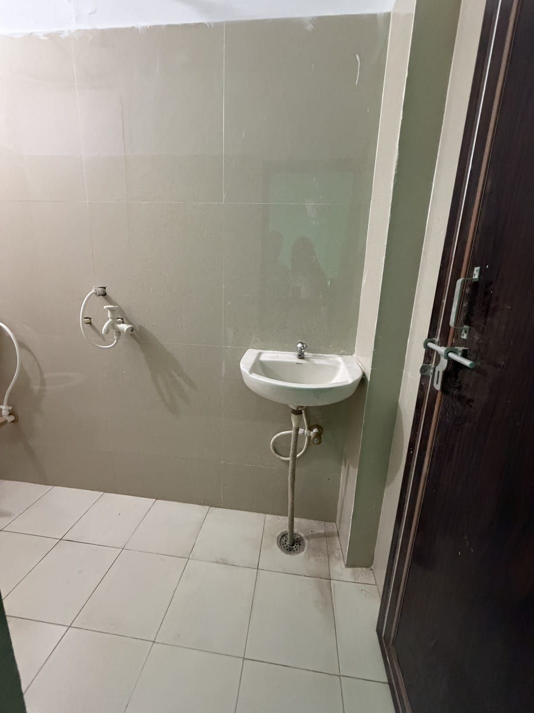 A bathroom with a white sink, a handheld showerhead, and a door with a handle.
