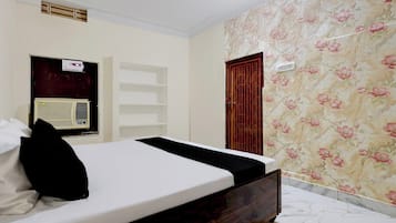 A bedroom with a bed, an air conditioning unit, a wardrobe, and a door.