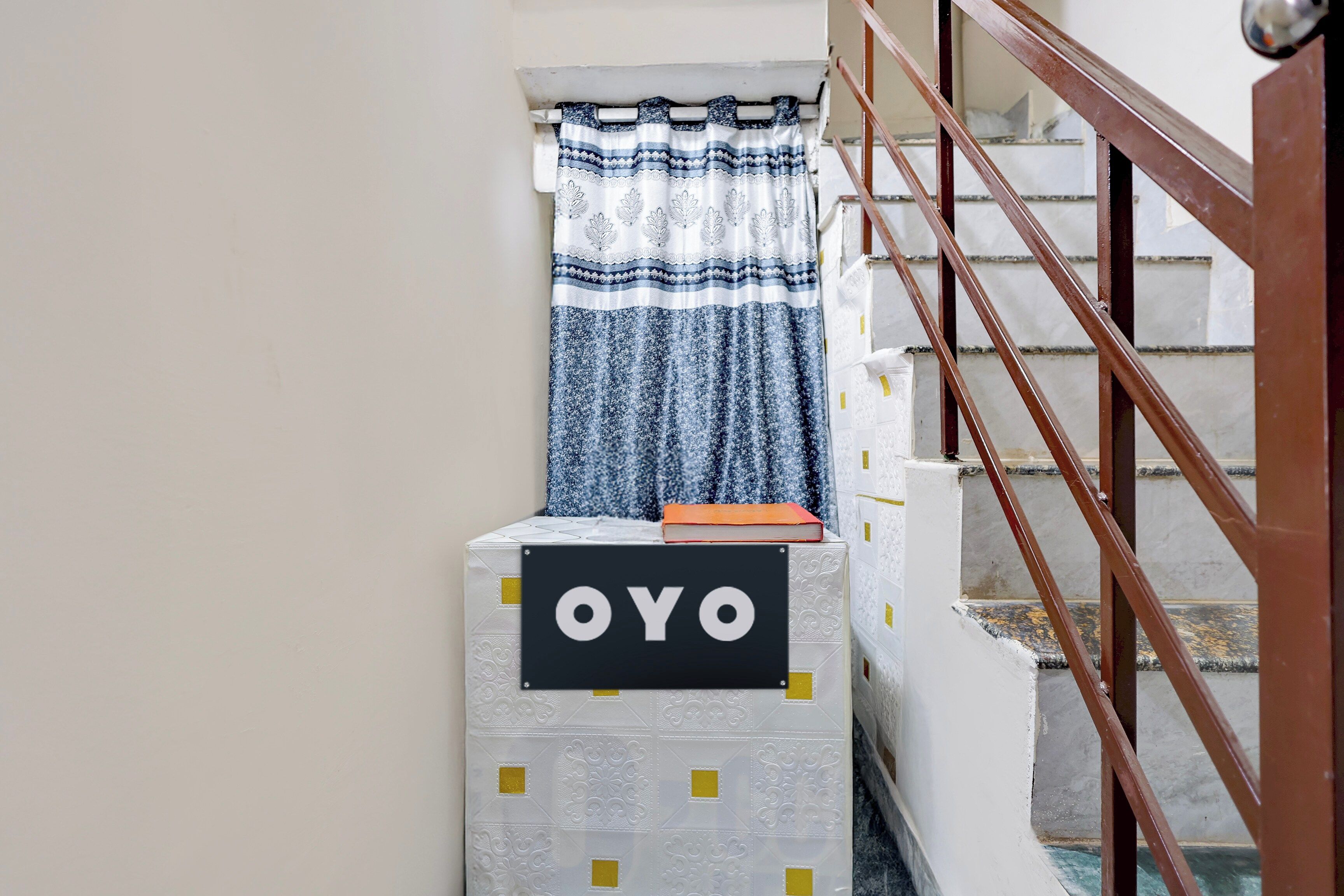 A staircase with a handrail, a sign with the letters 'OYO', and a patterned curtain.