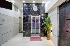 A modern elevator with a glass door, a digital display, and a marble wall with gold accents. - Hotel O ANANT ONE HOTEL AND BANQUETS (Ghaziabad)
