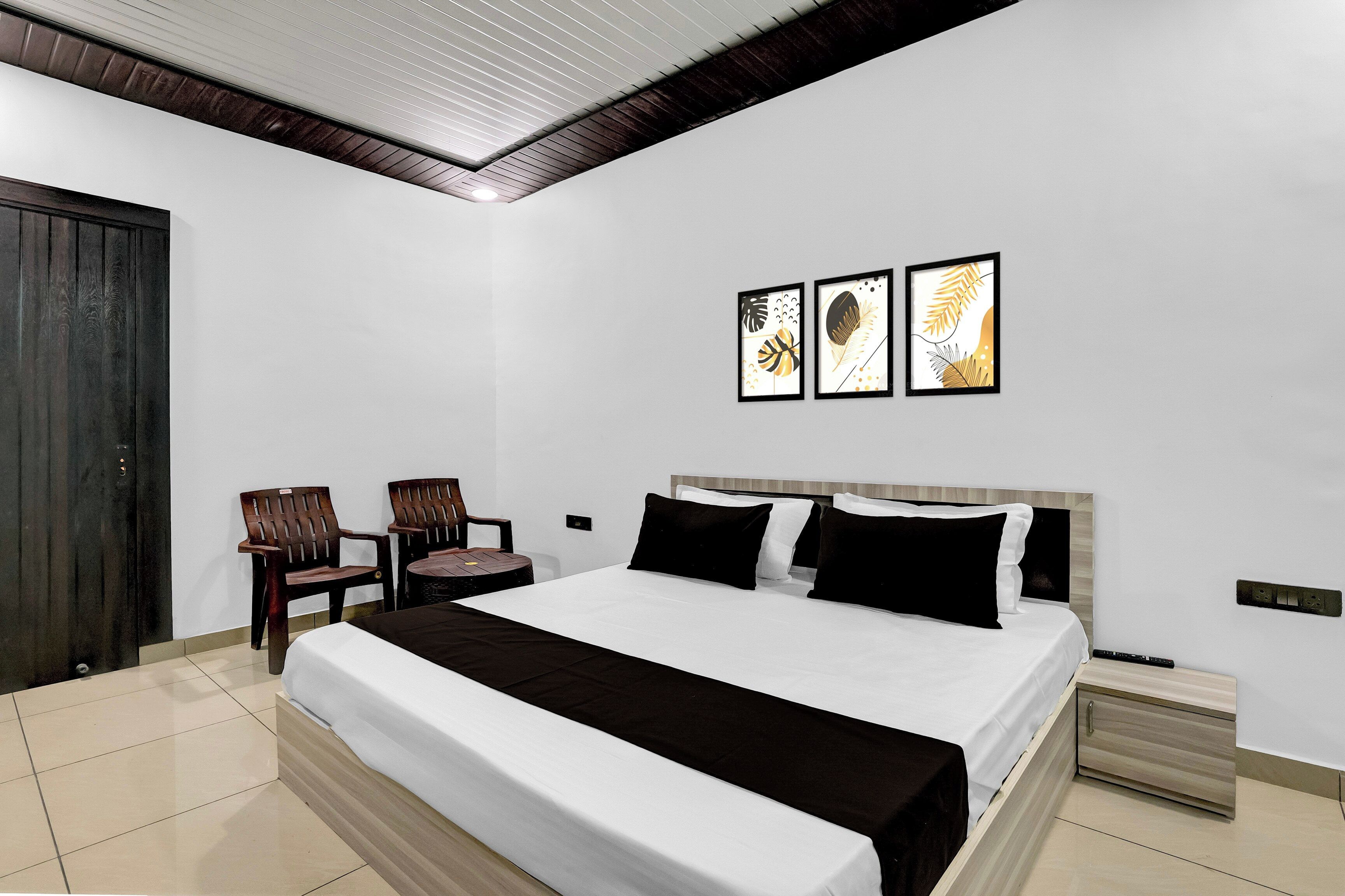 Habitación de hotel con una cama, dos sillas, una puerta de madera y obras de arte en la pared.