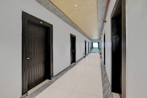 A hallway with doors on both sides, a tiled floor, and a ceiling with recessed lighting. - Hotel O Sukoon Guest House (Modinagar)