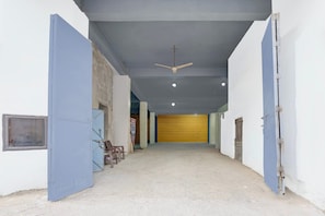 A hallway with a ceiling fan, a yellow door at the end, and a poster on the left wall. - Hotel O Sukoon Guest House (Modinagar)
