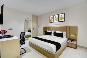 Habitación de hotel con cama, escritorio, silla, mesita de noche con teléfono y una obra de arte en la pared.