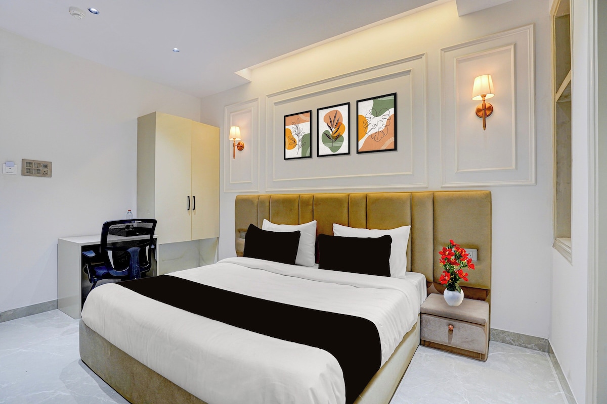 Una habitación de hotel con una cama grande, una mesita de noche con un jarrón de flores y una obra de arte en la pared.