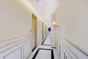 Corredor de hotel com portas, um luminário e uma porta azul no final.
