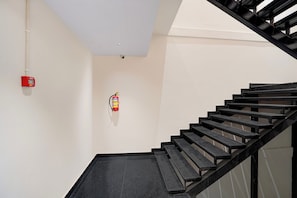 Una escalera con peldaños y barandillas negras, un detector de incendios en la pared y un detector de humo en el techo.