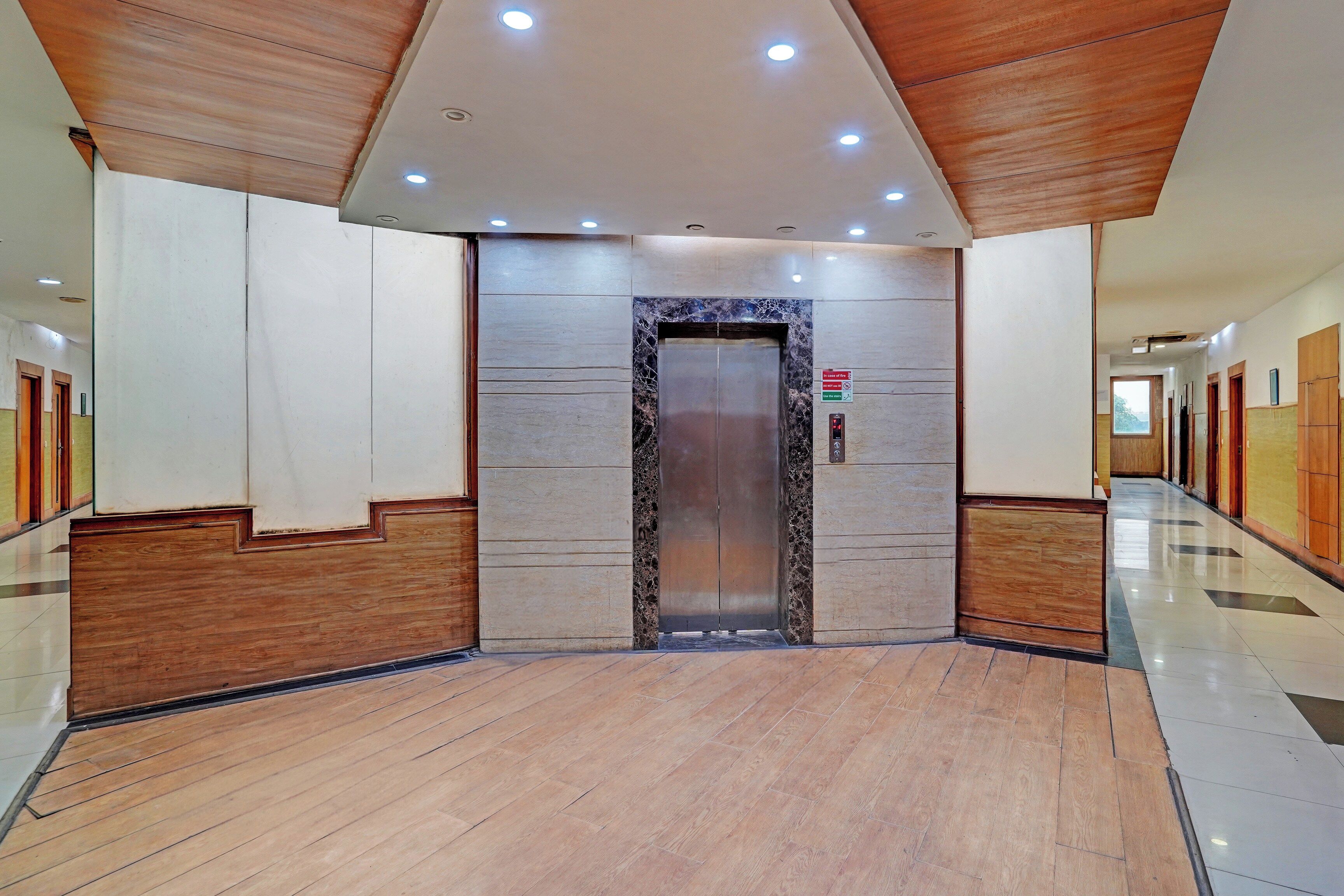 A modern elevator with a marble finish, flanked by wooden paneling and a polished floor.