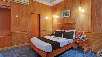 A hotel room with a wooden headboard, a bed with white bedding, a nightstand with a phone and a vase of flowers, and a picture on the wall.