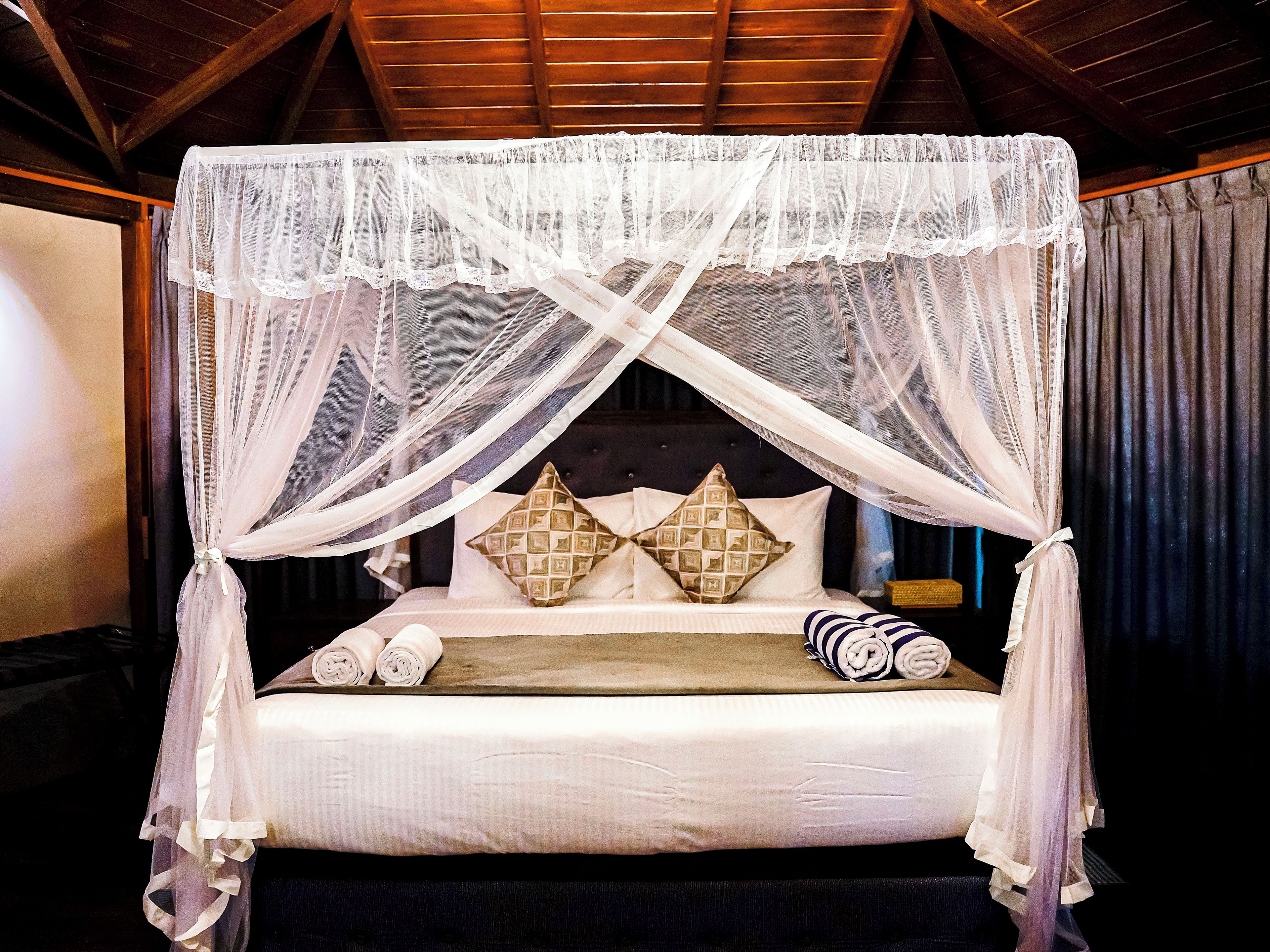 A four-poster canopy bed with a headboard, pillows, and rolled towels.