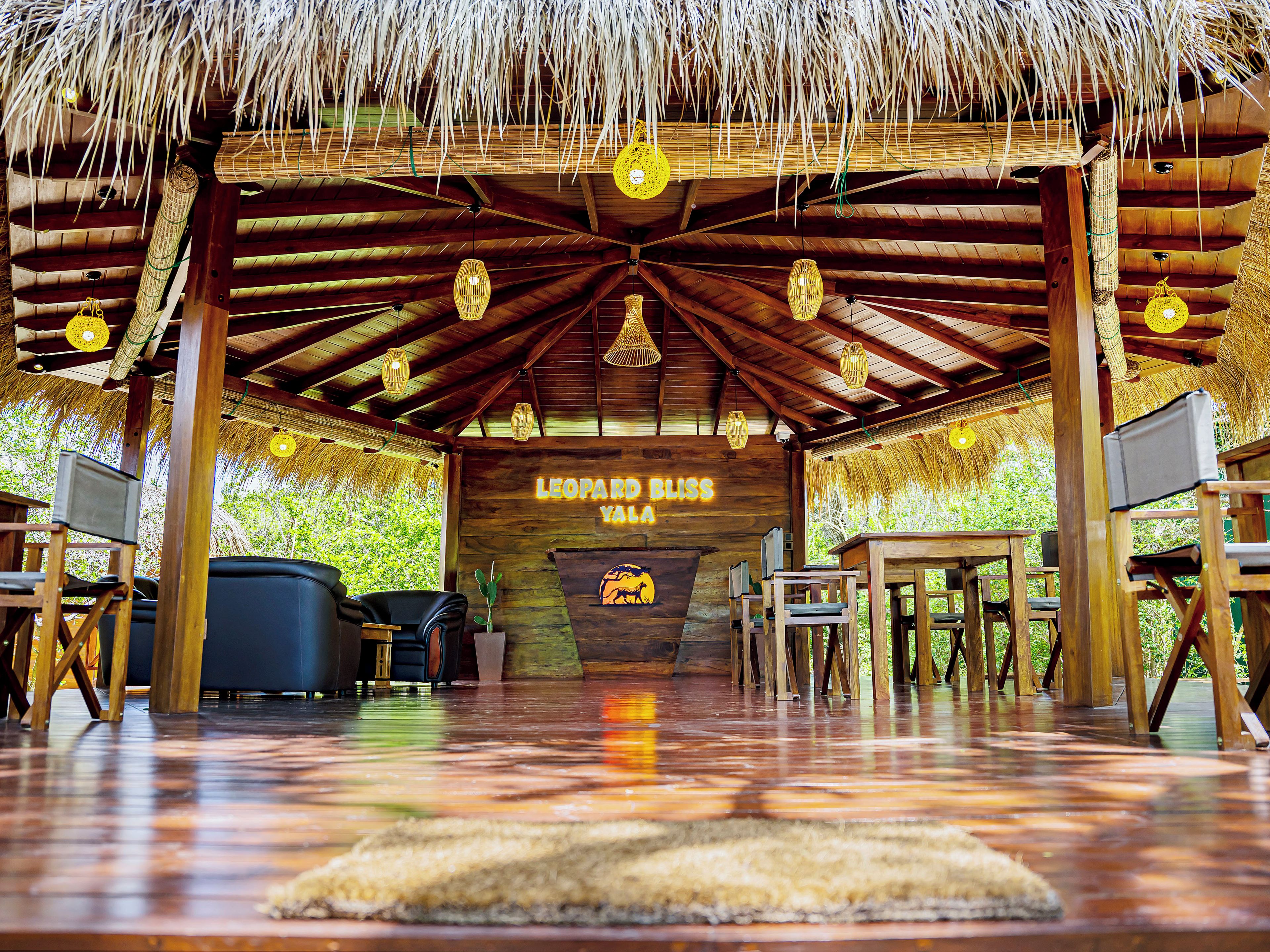 A wooden interior with a thatched roof, a sign reading 'LEOPARD BLISS YALAU', and a seating area with tables and chairs.