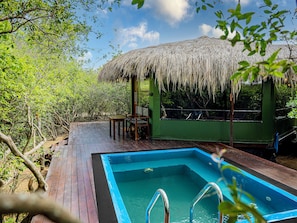 Un área de piscina con una estructura de techo de paja, terraza de madera y asientos.