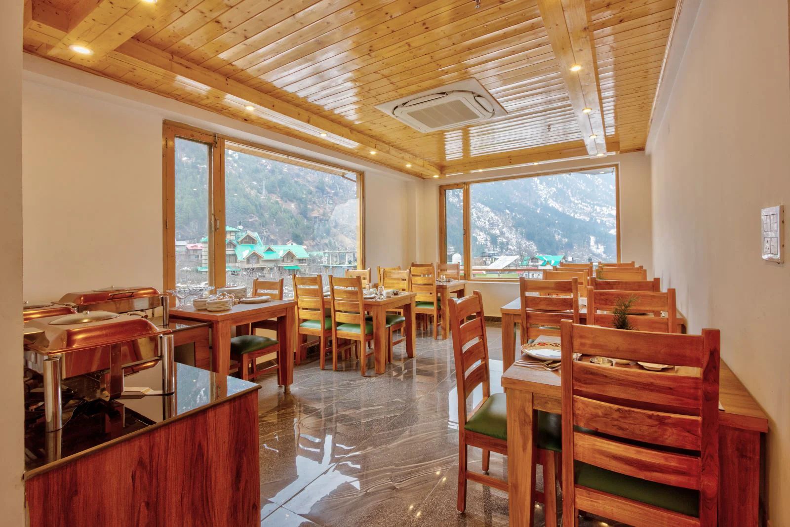 Un restaurante con muebles de madera y grandes ventanales que ofrecen vistas a las montañas.