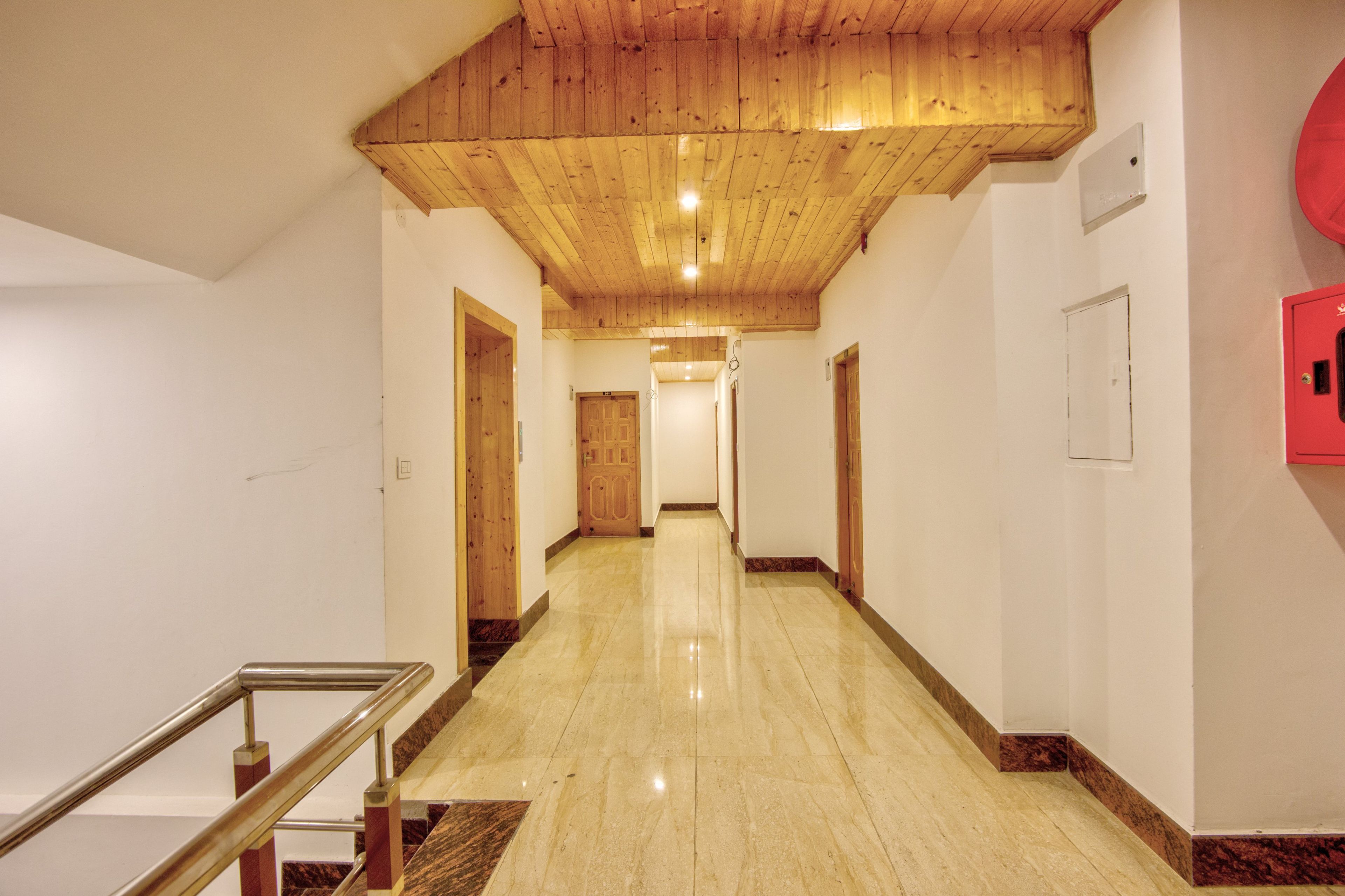 A hotel corridor with wooden ceiling, marble flooring, and a red emergency exit sign.
