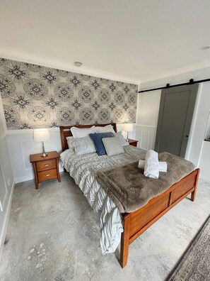 Un dormitorio con cama, mesitas de noche, papel tapiz estampado y una puerta.