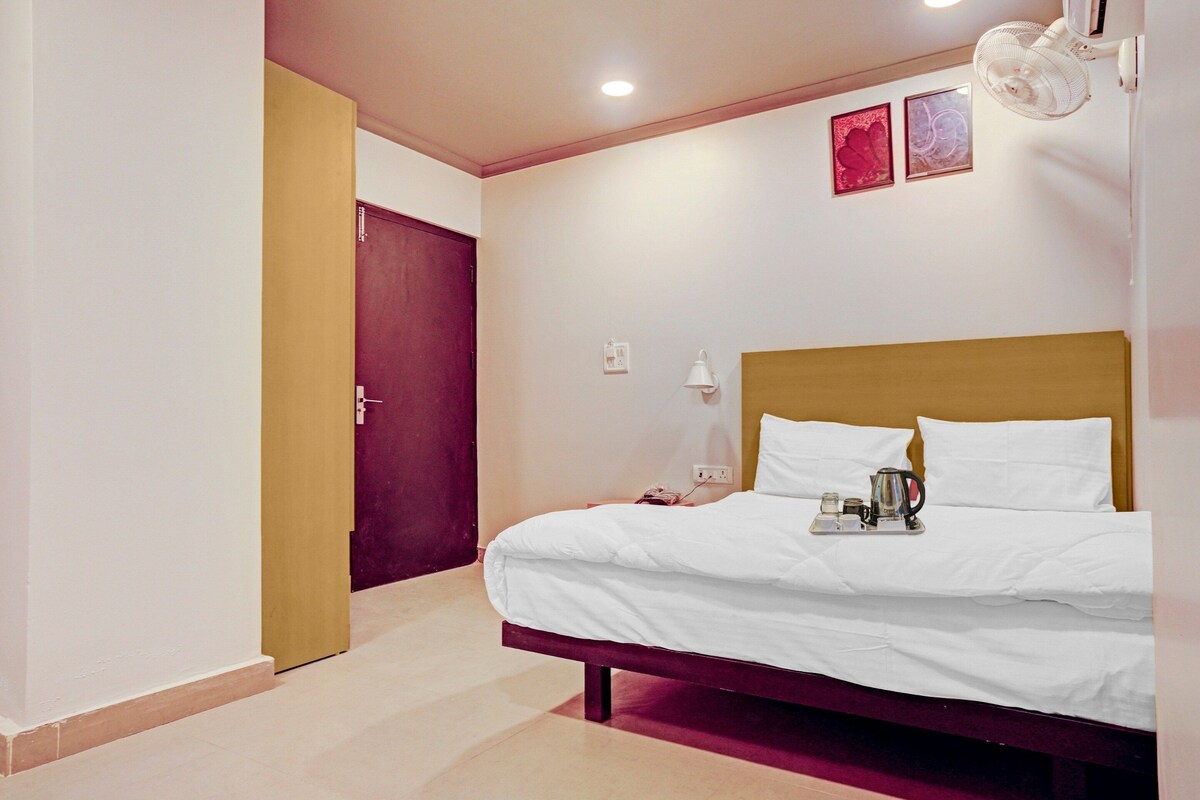 Una habitación de hotel con una cama, mesita de noche y un ventilador de pared.