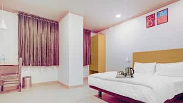 Habitación de hotel con cama, escritorio, silla, una mesita con bandeja, lámpara y dos cuadros en la pared.