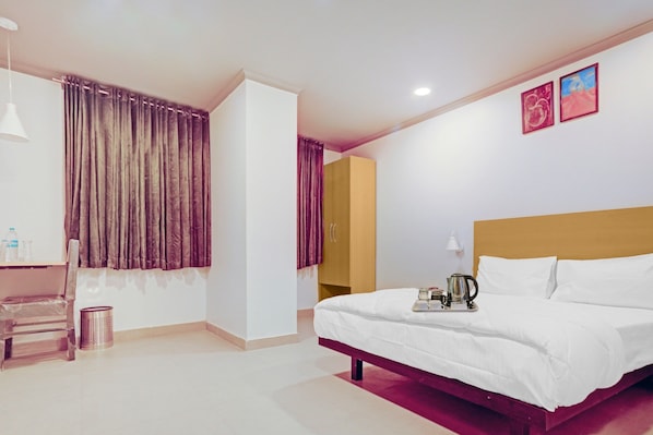A hotel room with a bed, a desk, a chair, a small table with a tray, a lamp, and two paintings on the wall. - Collection O by OYO One Hotel (Ghaziabad)