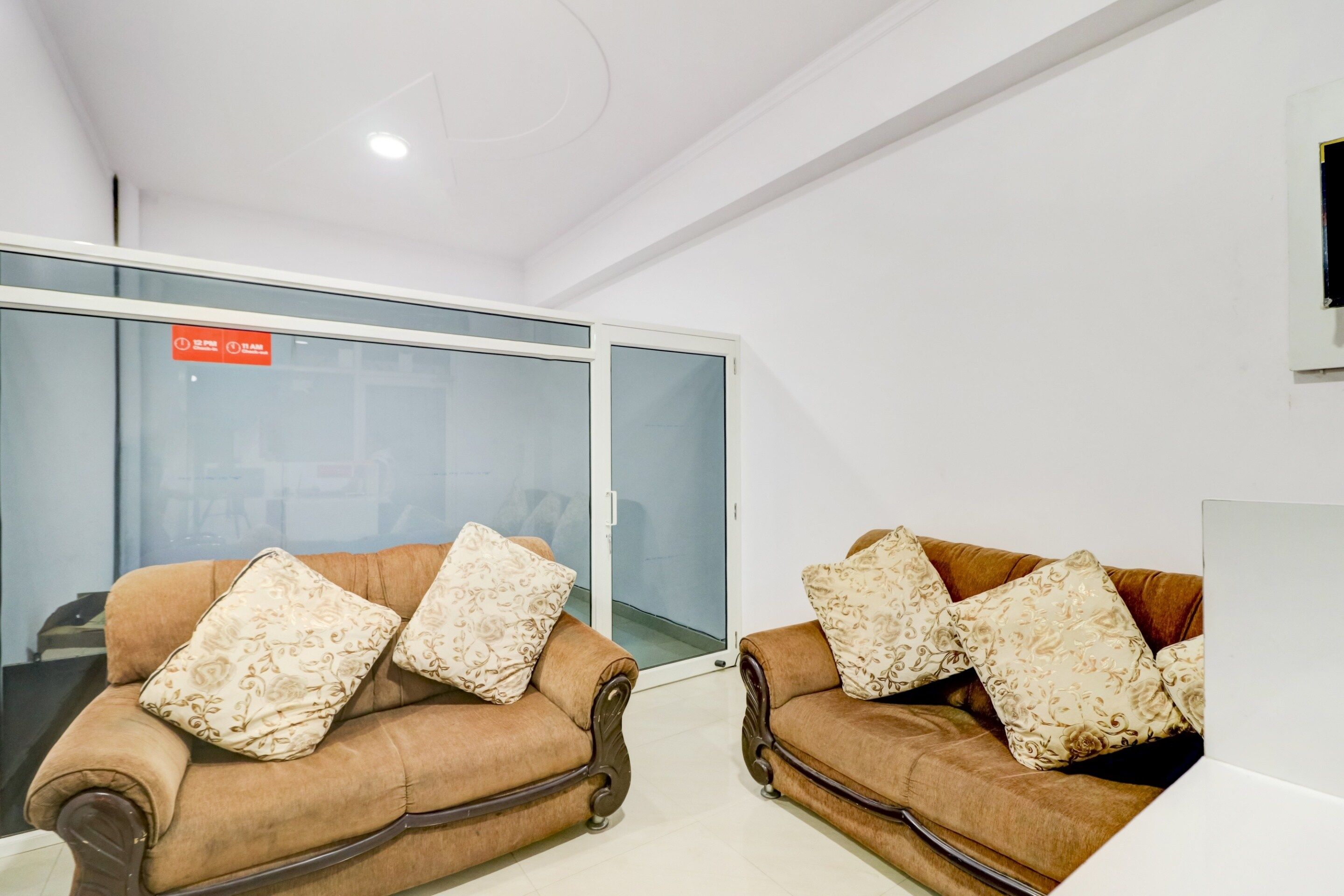 Two brown sofas with floral cushions in a modern office space with glass doors and a white ceiling.