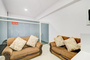 Two brown sofas with floral cushions in a modern office space with glass doors and a white ceiling. - Hotel O by OYO Ratan Pacific Hotel And (Ghaziabad)