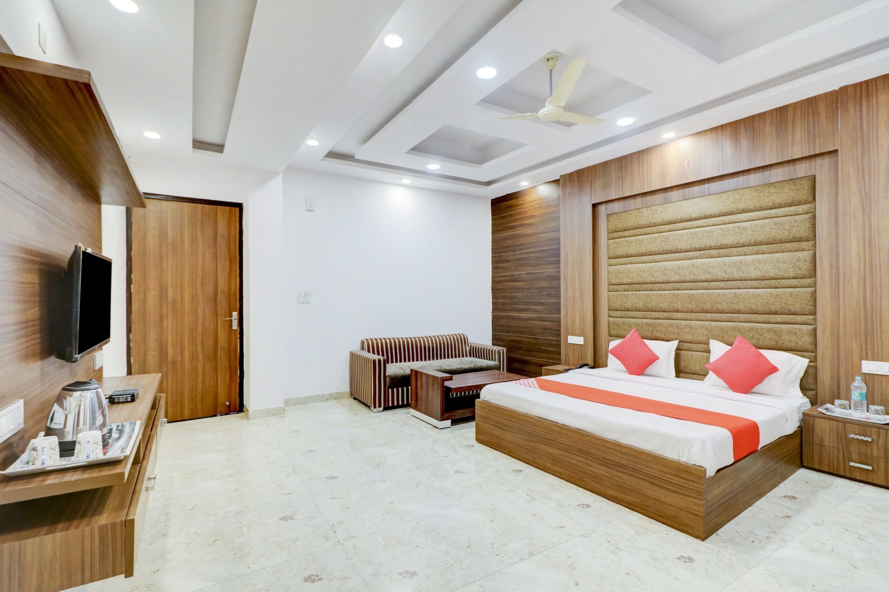 A hotel room with a bed, a sofa, a TV, a coffee maker, and a wooden wardrobe.