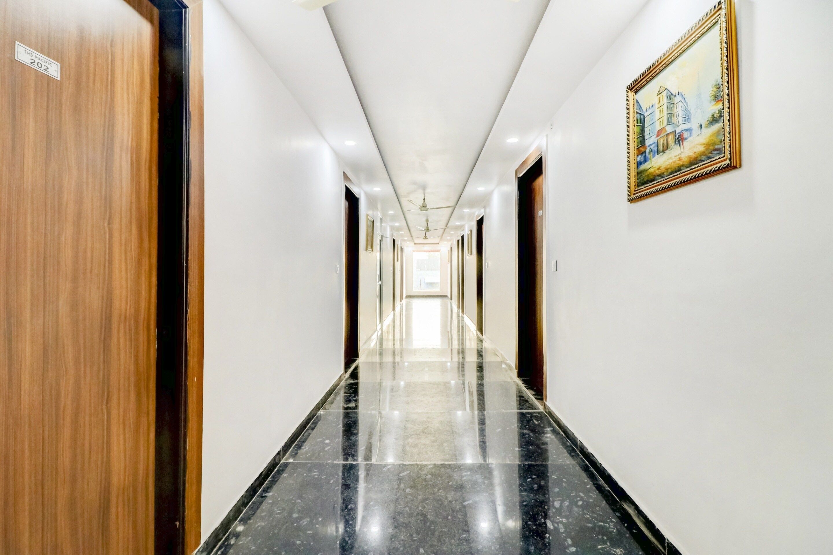A hotel hallway with a polished marble floor, wooden doors, and a framed painting on the wall.