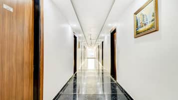 A hotel hallway with a polished marble floor, wooden doors, and a framed painting on the wall.