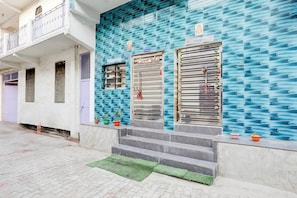 Edifício com fachada azul texturizada, área de recepção e escadaria que leva à entrada.