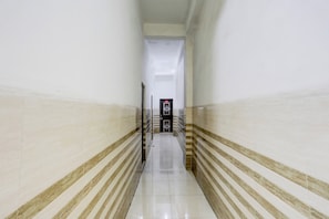 Um corredor com piso ladrilhado e paredes listradas, que leva a uma porta com teclado de segurança.