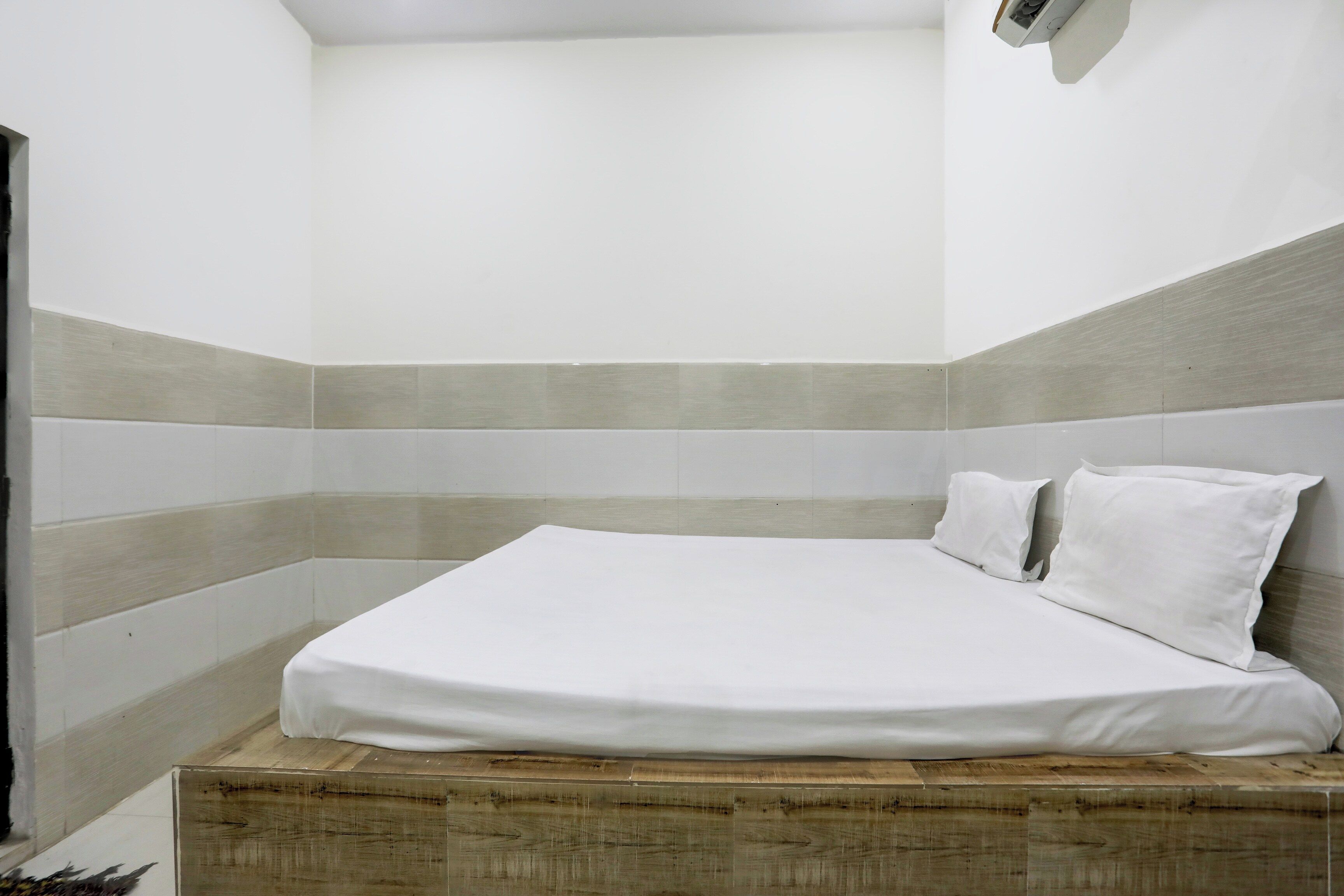 A single bed with white bedding in a corner room with a sloped ceiling and a light-colored wall.