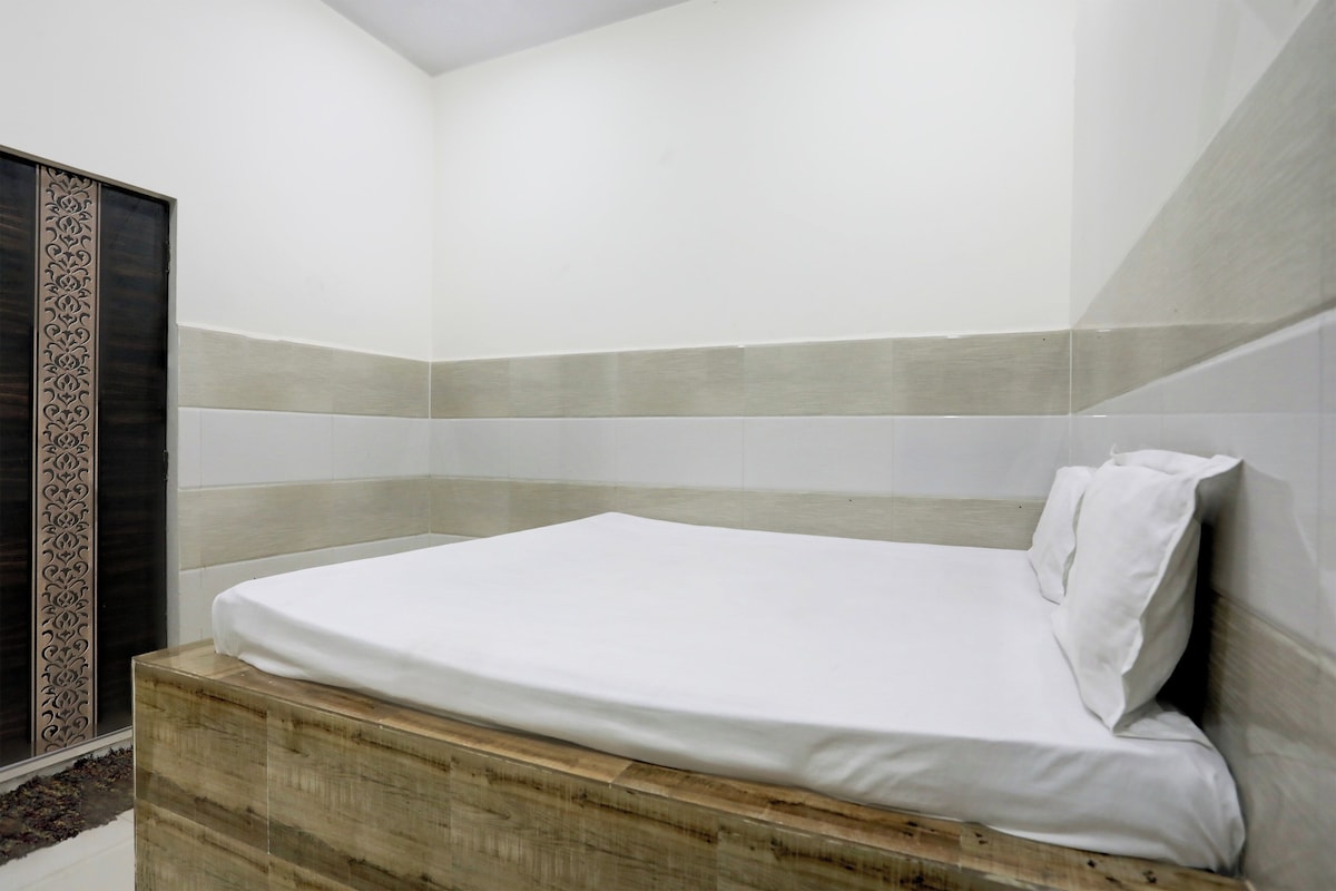 A single bed with a white mattress and pillow in a room with a wooden headboard and a decorative panel on the left.