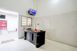 Uma área de recepção com televisão de tela plana na parede, um balcão de atendimento com um vaso de flores e uma janela com vista para o exterior.