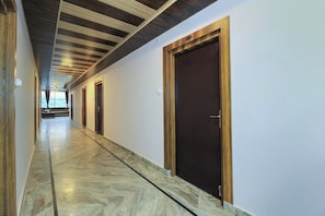 A hallway with wooden doors and a marble floor, leading to a room with a view. - Collection O Mehraz Residency (Haldwani)