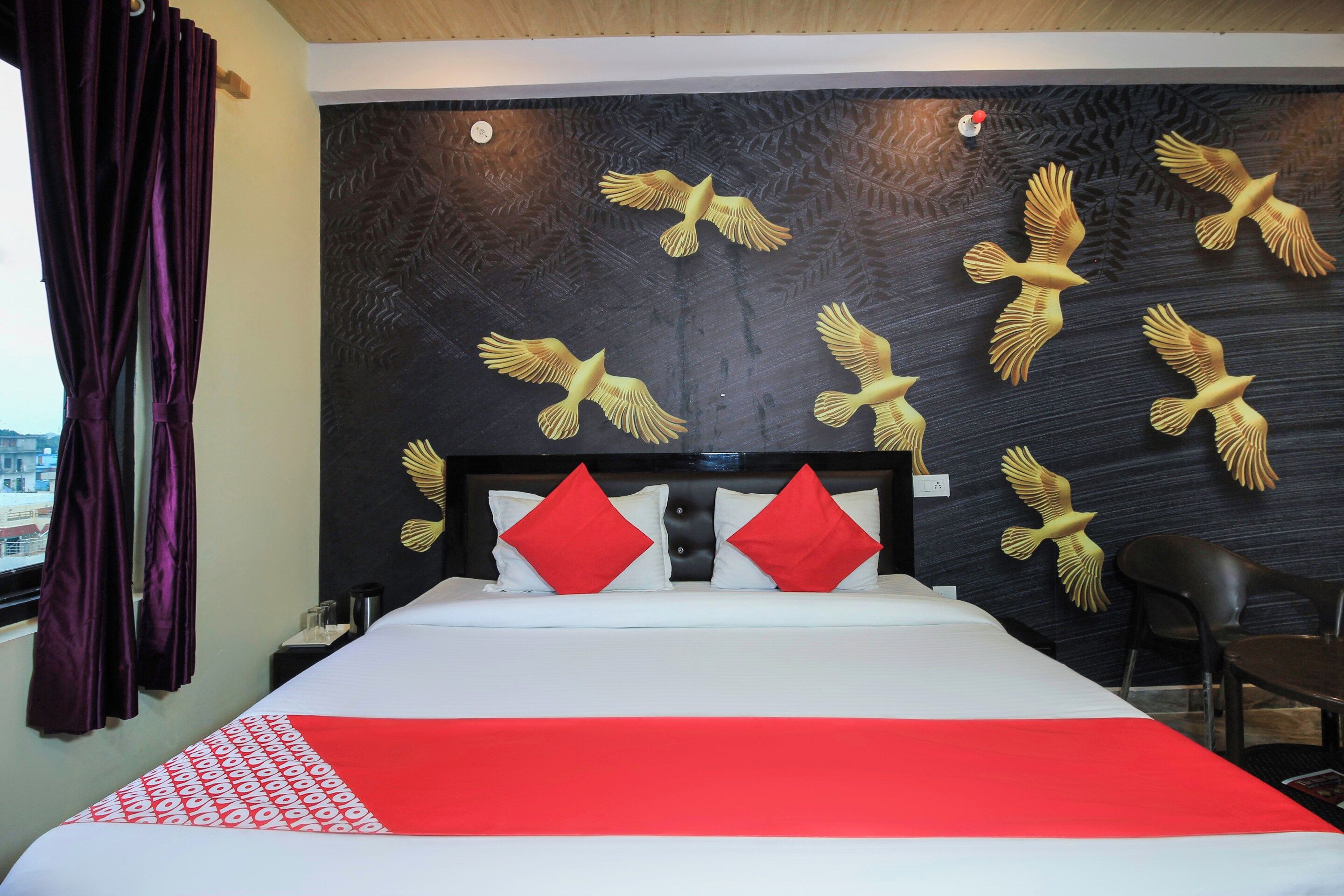 Ein Hotelzimmer mit einem Bett, roten Kissen, einem schwarzen Kopfteil und einer Wand mit goldenen Vogelornamenten.