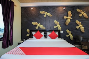Quarto de hotel com uma cama, almofadas vermelhas, cabeceira preta e uma parede decorada com pássaros dourados.