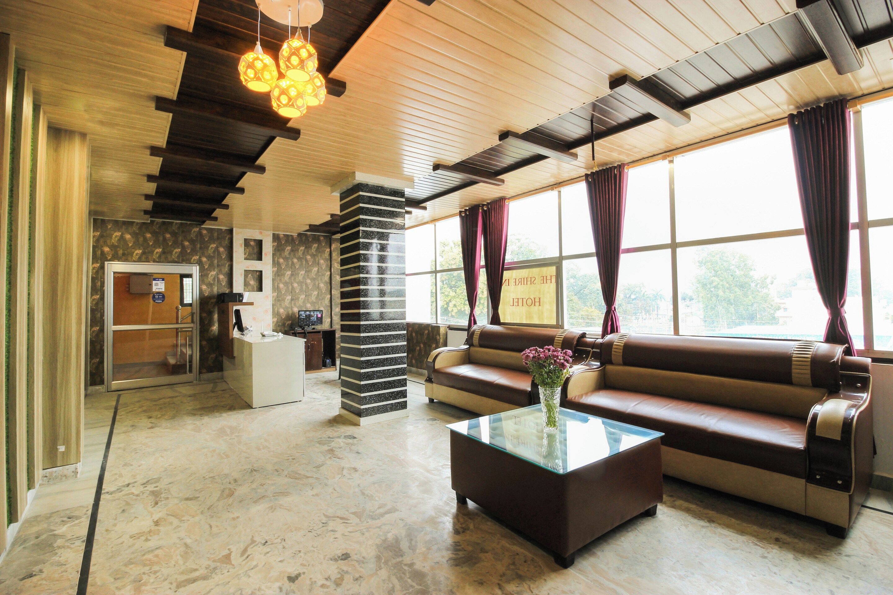 Eine Hotelhalle mit einer Rezeption, einer Couch, einem Couchtisch mit Blumen und einem großen Fenster mit Vorhängen.