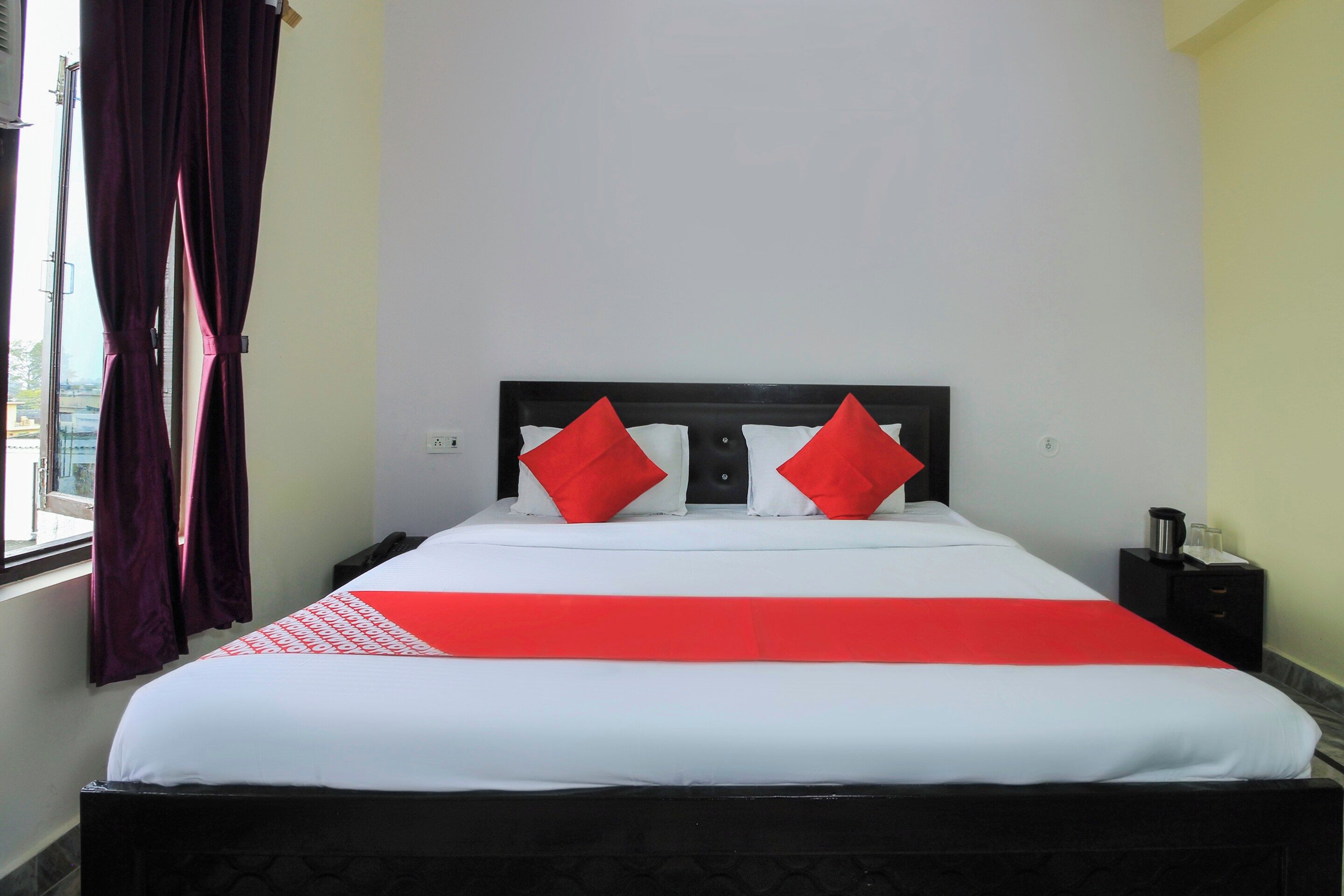 A hotel room with a bed, a nightstand, a window with curtains, and a view of the outside.