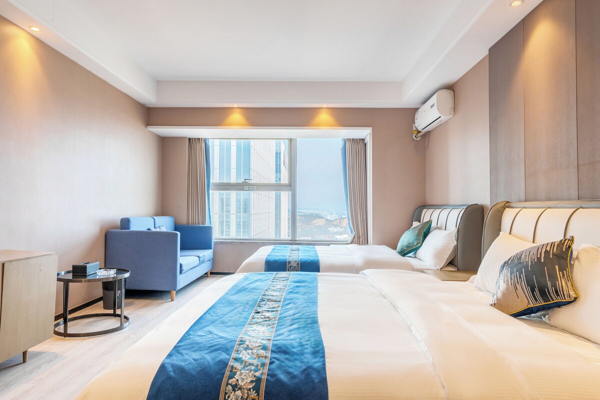 Ein Hotelzimmer mit einem großen Bett, einer Couch, einem kleinen Tisch und einem Fenster mit Blick auf die Stadt.