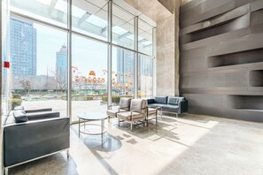 Ein modernes Interieur mit einem großen Glasfenster, einer Sitzecke mit Sofas und einem kleinen Tisch sowie einer Wand mit geometrischem Design.