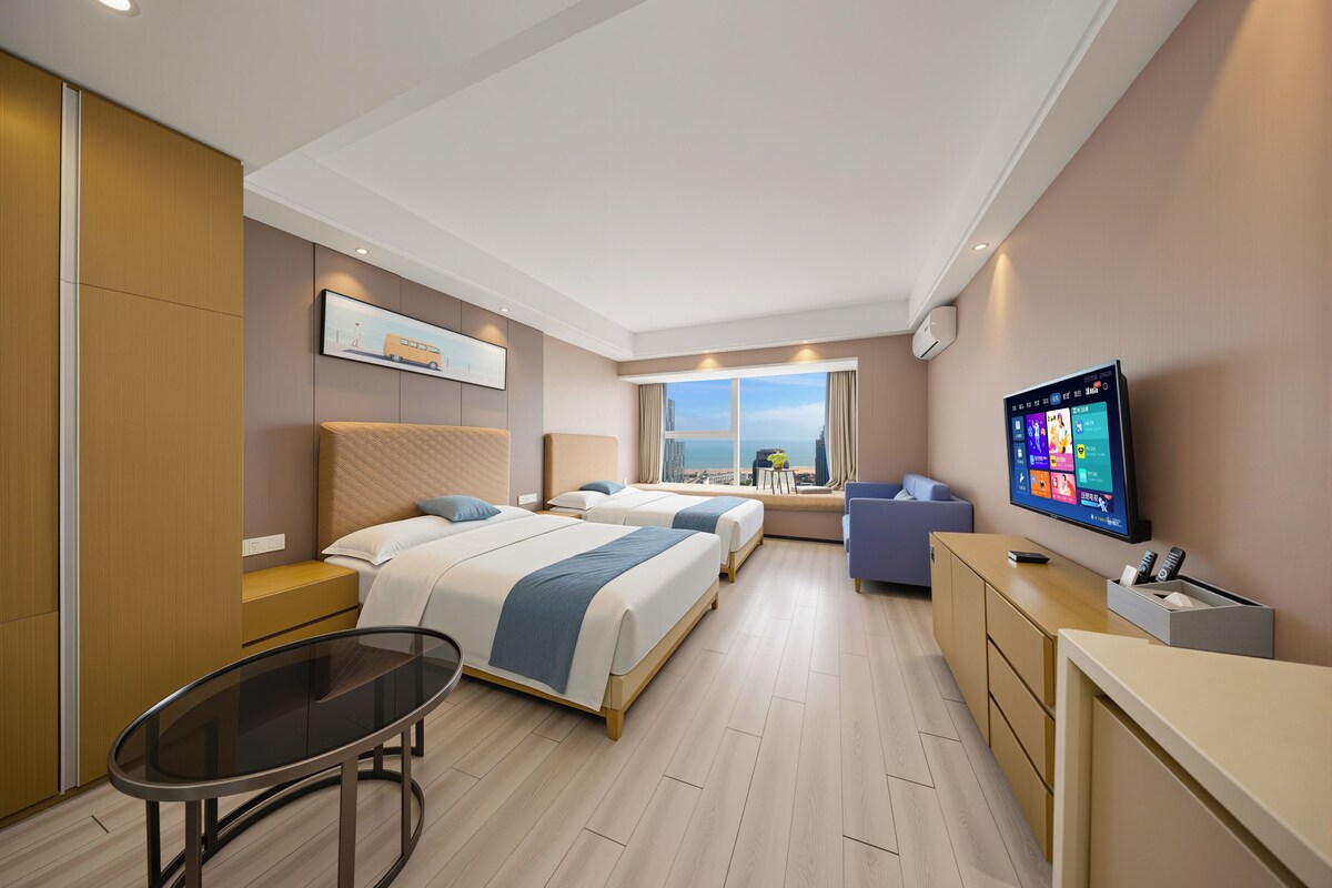 Ein Hotelzimmer mit zwei Betten, einem Fernseher, einem Schreibtisch und Blick auf die Stadt.