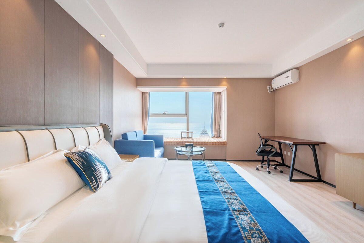 Ein Hotelzimmer mit Bett, Schreibtisch, Stuhl, Fenster mit Aussicht und Klimaanlage.