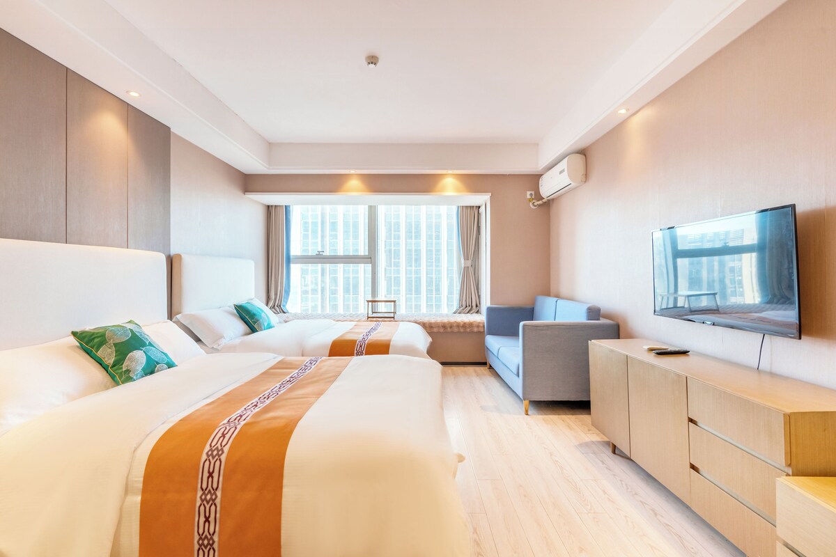 Ein Hotelzimmer mit zwei Betten, einem Sofa, einem Fernseher und einem Fenster mit Vorhängen.
