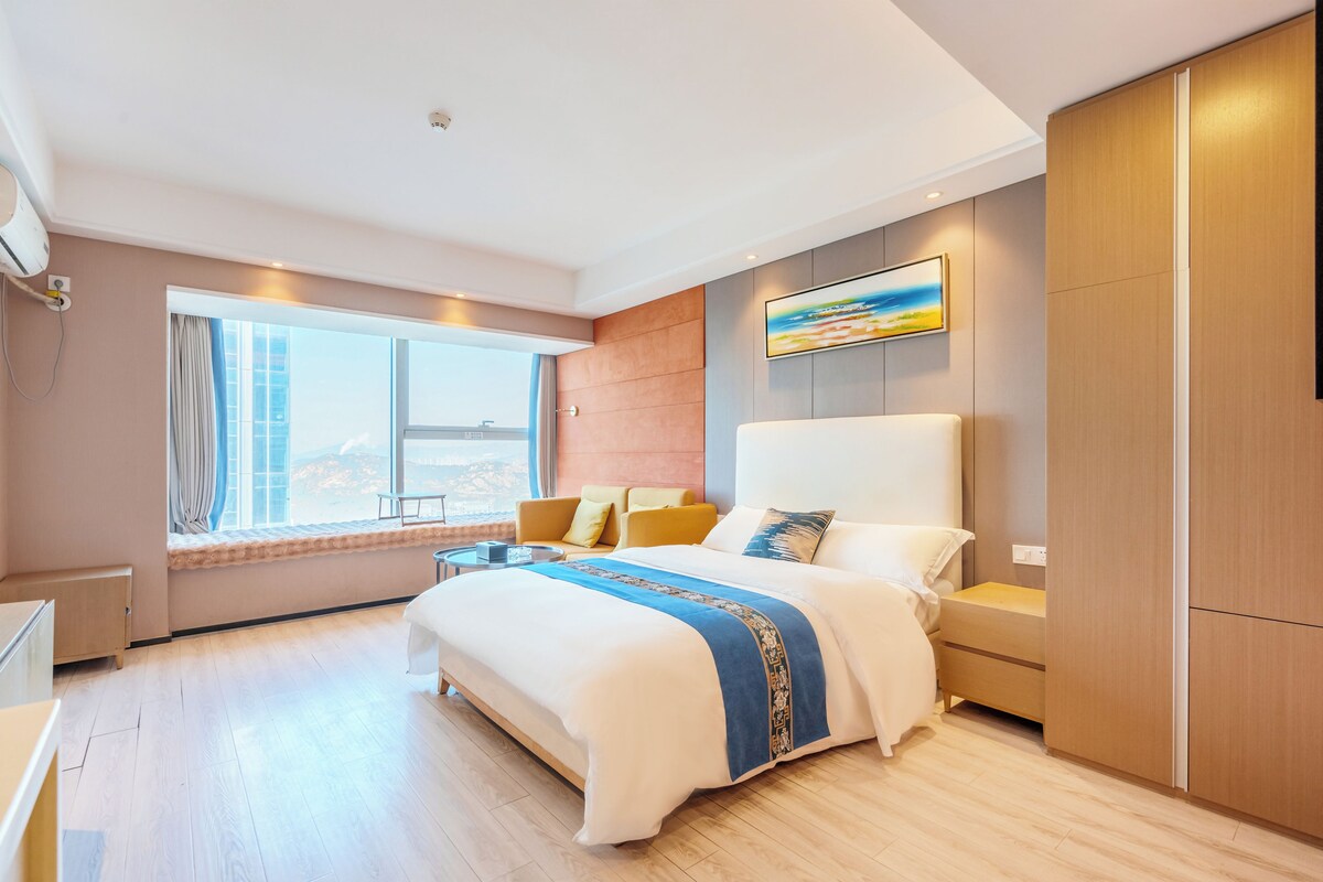 Ein modernes Hotelzimmer mit einem großen Bett, einem Fenster mit Ausblick, einem Gemälde an der Wand und einem Kleiderschrank.