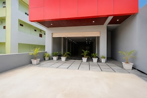 Entrada de un edificio moderno con un alero rojo, plantas en macetas y suelo de baldosas.