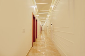 Un pasillo largo y bien iluminado con piso brillante, puertas a la izquierda y una pared lisa a la derecha.