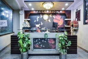 A reception desk with a clock, a sign reading 'RECEPTION', and a wall with a floral pattern. - Hotel O Alpen Rose (Haridwar)