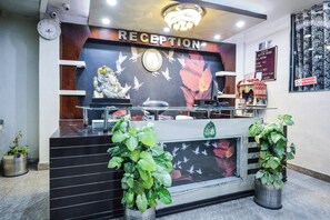 A reception desk with a clock, a statue, and a sign indicating a check-out time. - Hotel O Alpen Rose (Haridwar)