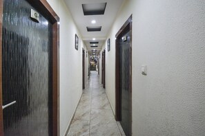 A corridor with doors on both sides, a tiled floor, and recessed lighting on the ceiling. - Hotel O Alpen Rose (Haridwar)