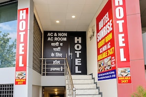 Entrada de hotel con opciones de habitaciones con aire acondicionado y sin aire acondicionado, una escalera y un cartel que indica disponibilidad de habitaciones las 24 horas, los 7 días de la semana.